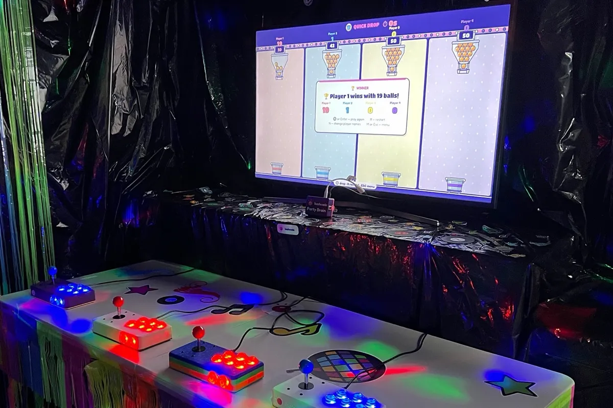 Our son's birthday party: a TV showing the Quick Drop game, and the four Bashcade controllers on a party table under coloured lights